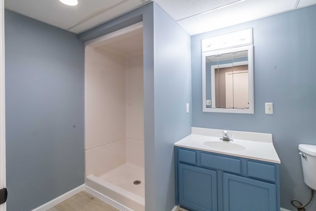 full bath featuring toilet, wood finished floors, vanity, baseboards, and a stall shower