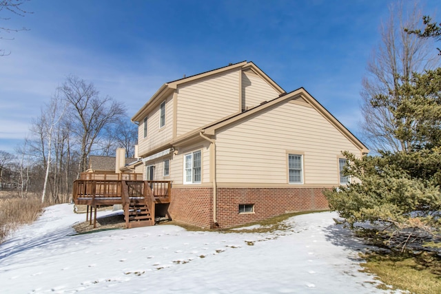 snow covered property featuring brick siding and a deck