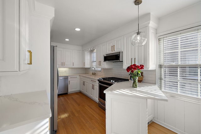 kitchen featuring sink, backsplash, pendant lighting, stainless steel appliances, and white cabinets