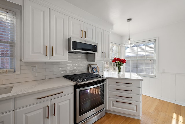 kitchen featuring stainless steel appliances, light stone counters, white cabinets, light hardwood / wood-style floors, and pendant lighting