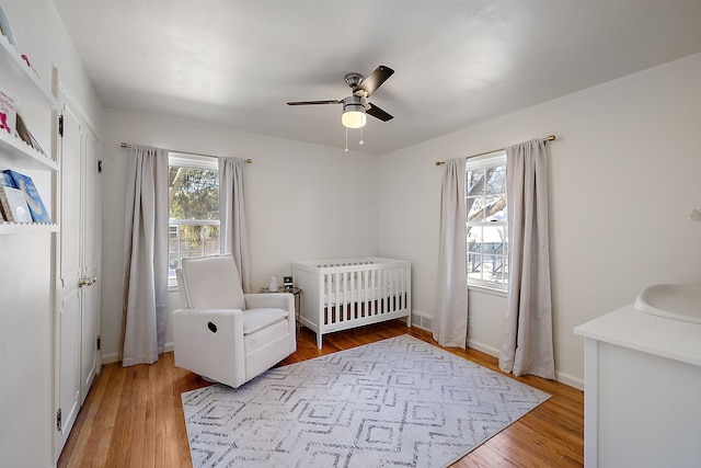 bedroom featuring ceiling fan, multiple windows, a nursery area, and hardwood / wood-style floors