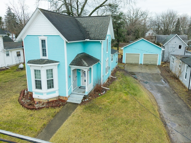 victorian-style house with a shingled roof, a detached garage, an outbuilding, and a front yard