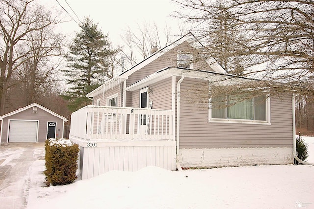 view of snow covered exterior featuring a garage, an outbuilding, driveway, and a balcony