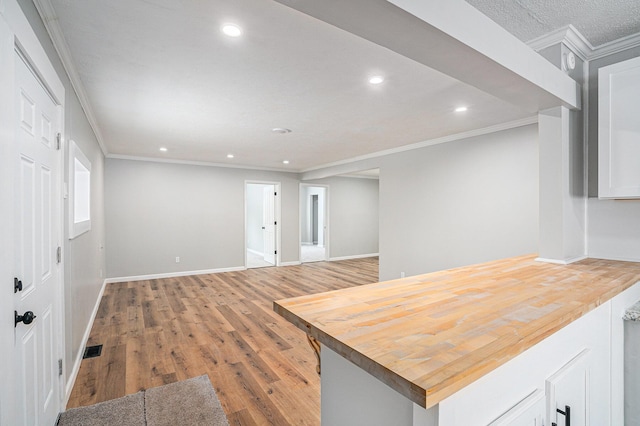 kitchen featuring visible vents, baseboards, open floor plan, light wood finished floors, and crown molding