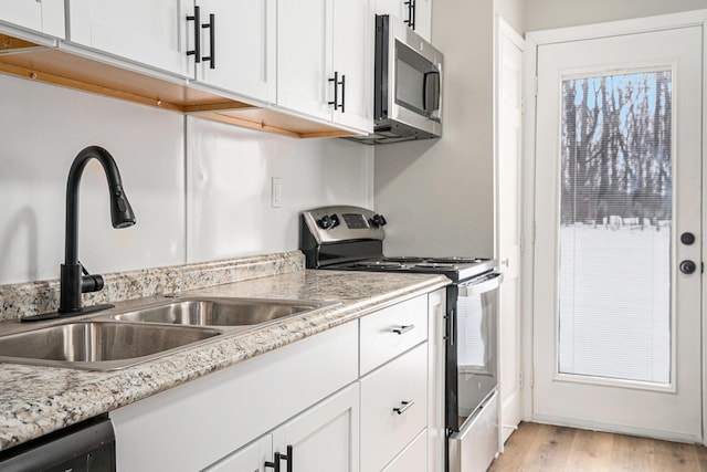 kitchen with stainless steel appliances, light wood-style flooring, white cabinetry, a sink, and light stone countertops