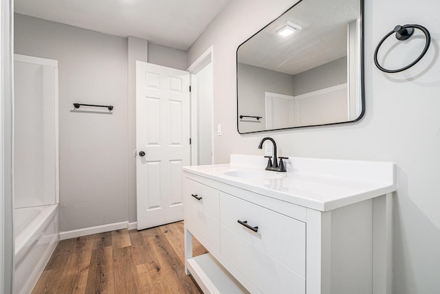 bathroom featuring a tub, wood finished floors, vanity, and baseboards