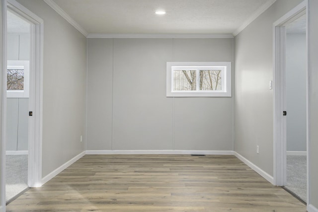 empty room featuring light wood-style floors, baseboards, and crown molding