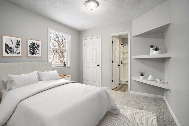 bedroom with light carpet, a textured ceiling, baseboards, and ensuite bathroom