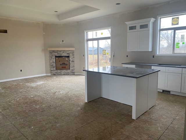 kitchen with a center island, a raised ceiling, white cabinetry, and a fireplace