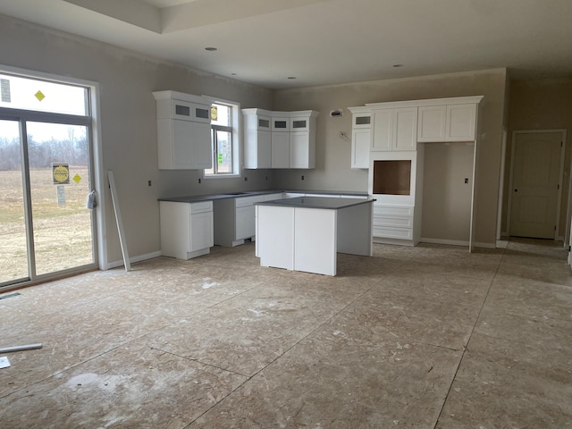 kitchen featuring a kitchen island, white cabinetry, baseboards, dark countertops, and glass insert cabinets