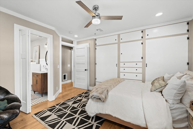 bedroom with light wood-type flooring, ornamental molding, and ensuite bath