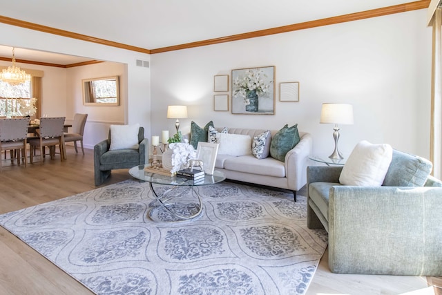 living area with visible vents, crown molding, baseboards, wood finished floors, and a notable chandelier