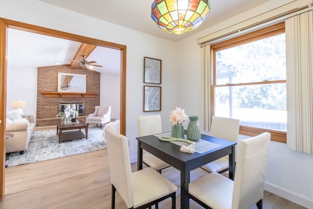 dining room with baseboards, light wood-style floors, a brick fireplace, and vaulted ceiling with beams