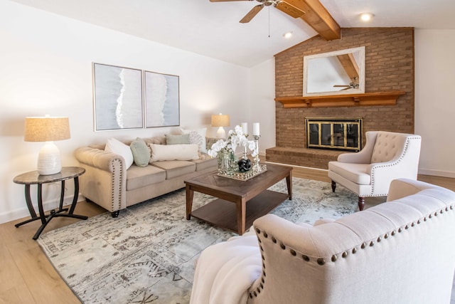 living room with lofted ceiling with beams, wood finished floors, baseboards, a brick fireplace, and ceiling fan