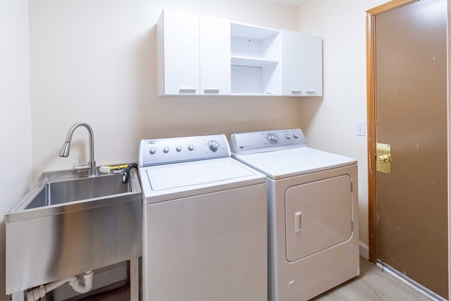 clothes washing area with washer and dryer, a sink, cabinet space, light wood finished floors, and baseboards