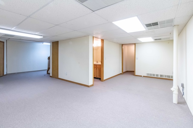 finished below grade area featuring a paneled ceiling, visible vents, baseboards, and light colored carpet