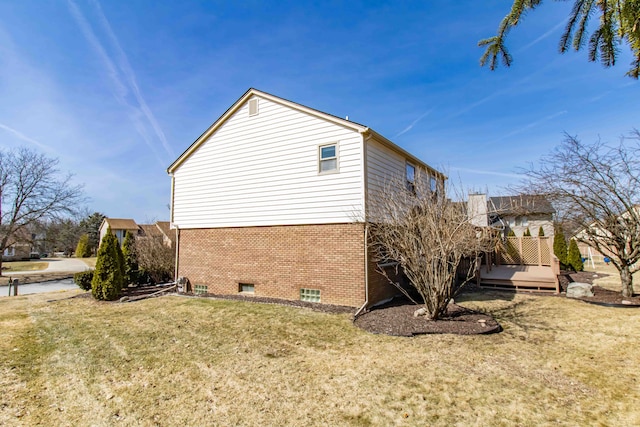 view of side of property with brick siding, a deck, and a yard