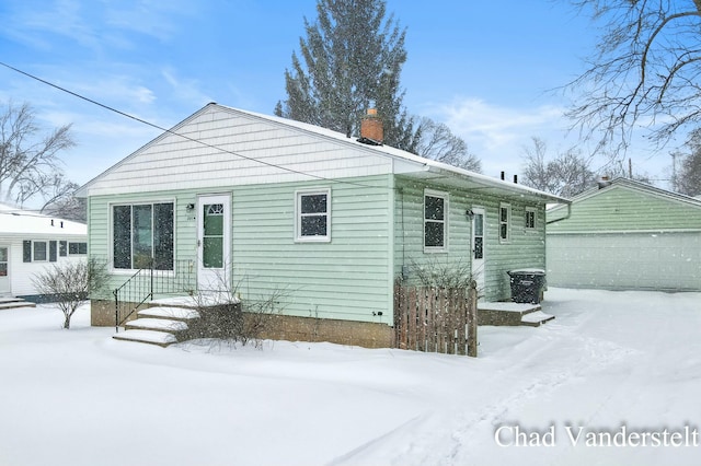 snow covered rear of property featuring a garage and an outbuilding