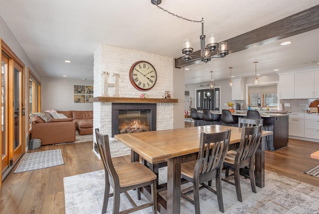 dining area featuring light wood-type flooring, a brick fireplace, and a chandelier