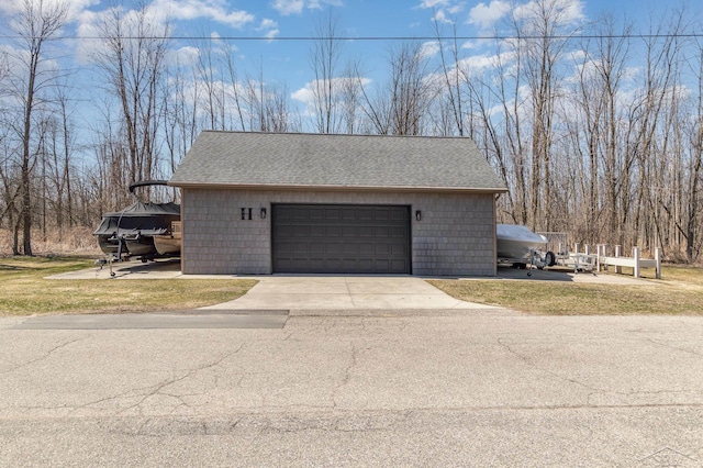 view of side of property with a shingled roof, a garage, concrete driveway, and an outdoor structure