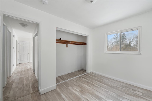 unfurnished bedroom with light wood-type flooring, a closet, and baseboards