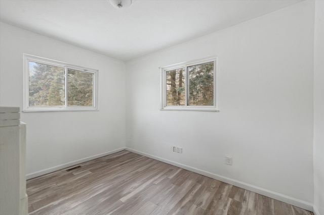 unfurnished room with baseboards, a healthy amount of sunlight, visible vents, and light wood finished floors