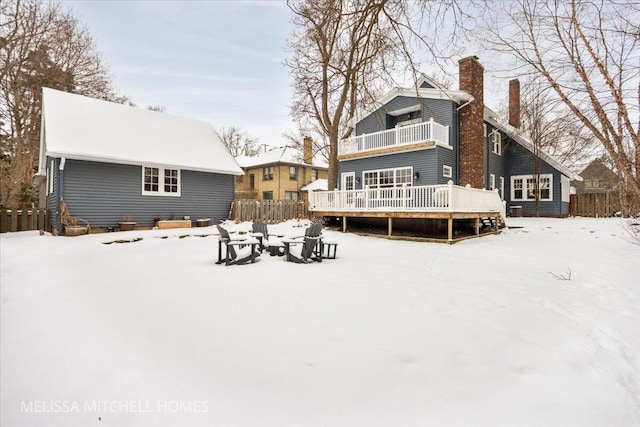 snow covered back of property with a balcony and a wooden deck