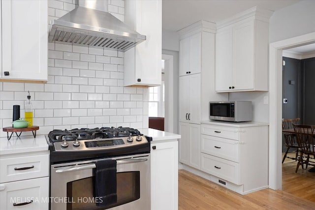 kitchen featuring light wood-type flooring, stainless steel appliances, white cabinetry, and extractor fan