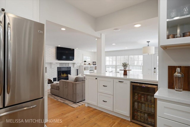 kitchen with light wood-type flooring, a fireplace, stainless steel fridge, white cabinets, and beverage cooler