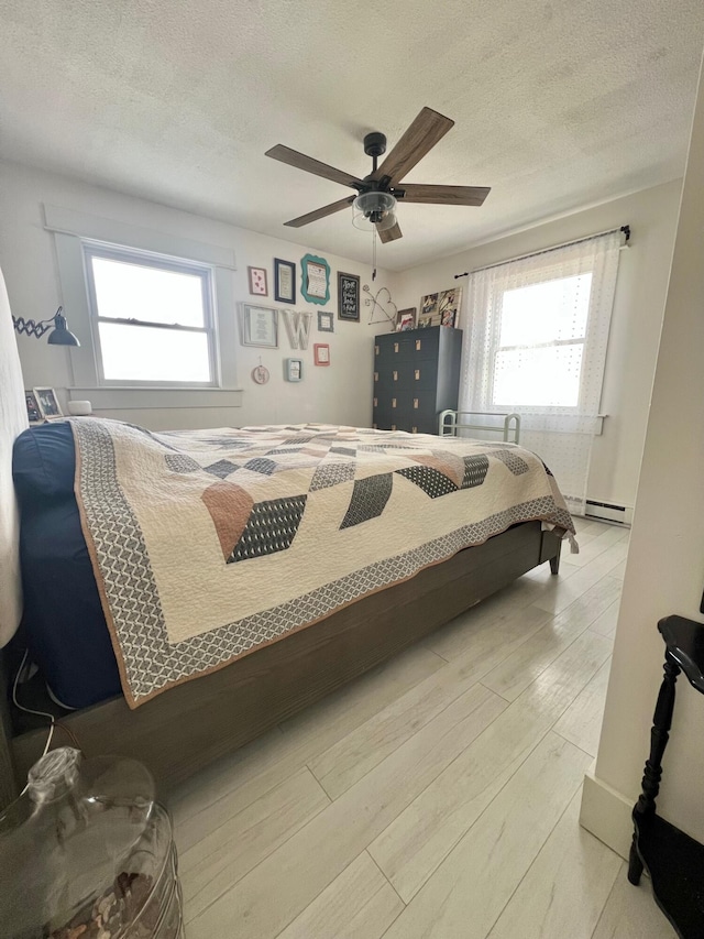 bedroom featuring light wood-type flooring, a baseboard radiator, a textured ceiling, and a ceiling fan