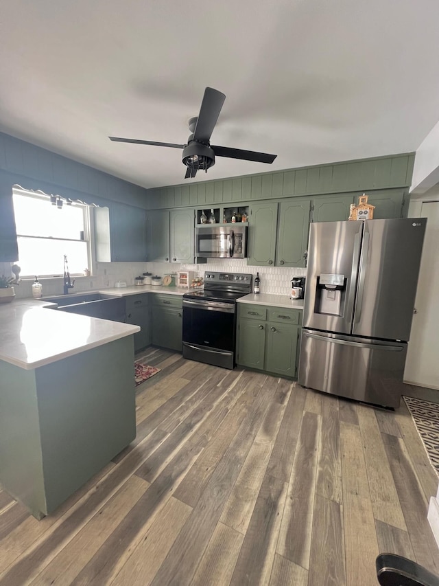 kitchen with dark wood-type flooring, a sink, light countertops, appliances with stainless steel finishes, and green cabinetry