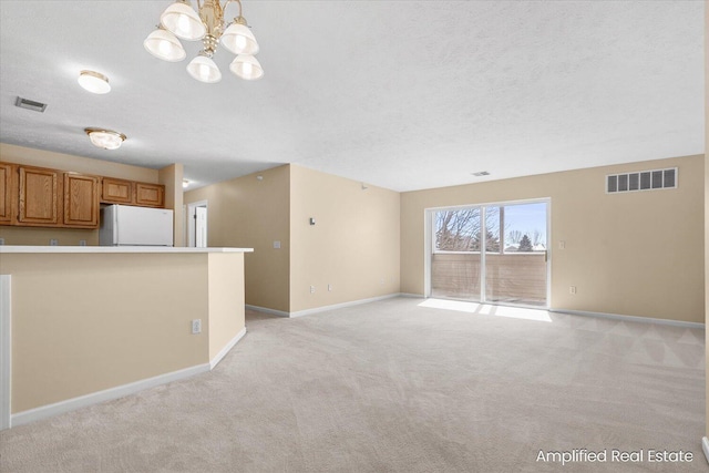 unfurnished living room with a textured ceiling, a chandelier, and light colored carpet