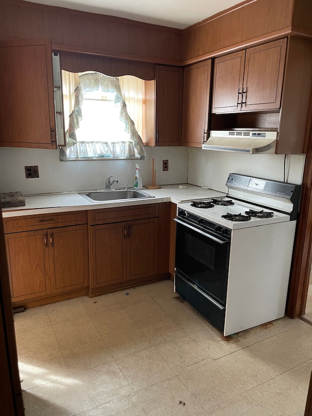 kitchen with under cabinet range hood, brown cabinets, gas range gas stove, light countertops, and a sink