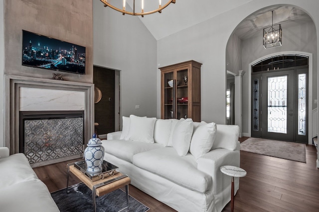 living room with arched walkways, high vaulted ceiling, a fireplace, dark wood-style floors, and an inviting chandelier