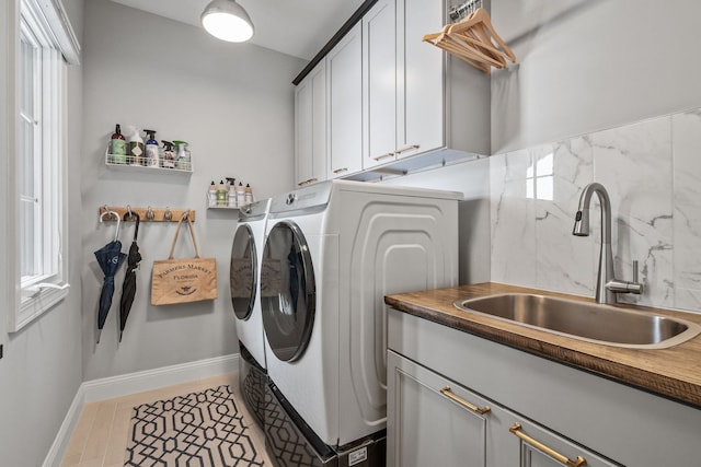 laundry area with washing machine and dryer, cabinet space, a sink, and baseboards