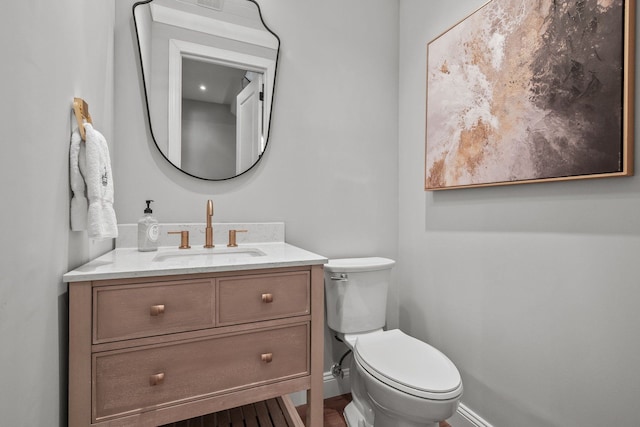 half bath with toilet, baseboards, and vanity