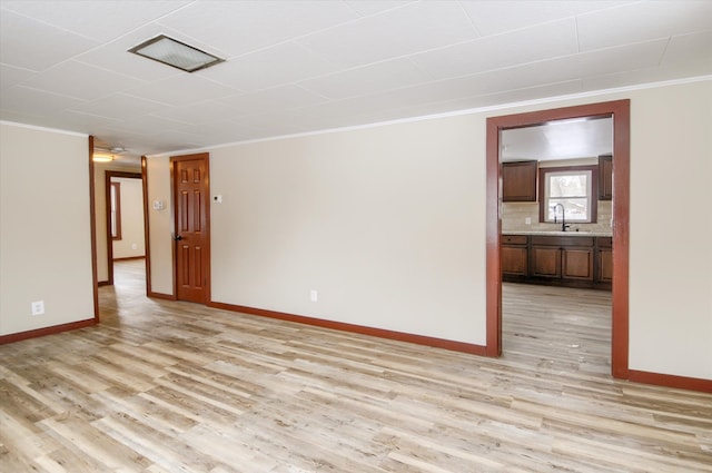 empty room featuring baseboards, light wood-type flooring, and crown molding