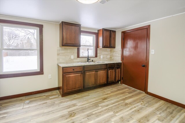 kitchen with light stone counters, light wood-style flooring, a sink, baseboards, and tasteful backsplash