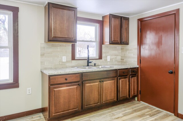 kitchen featuring tasteful backsplash, light wood-type flooring, a sink, and baseboards