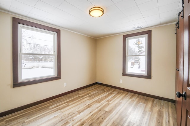 empty room featuring visible vents, light wood-style flooring, a barn door, ornamental molding, and baseboards