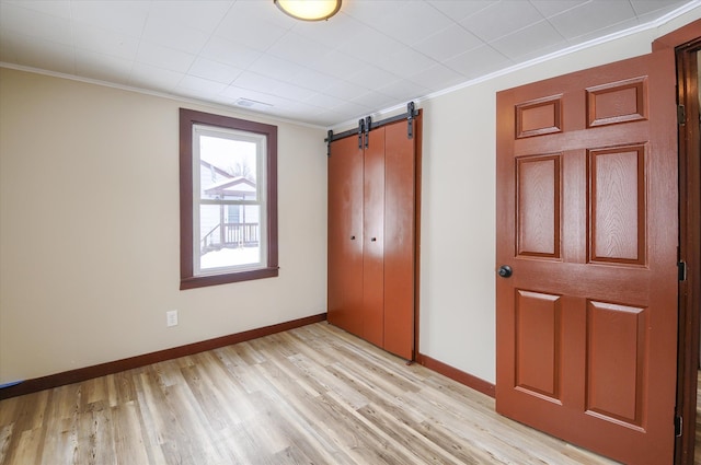 unfurnished bedroom featuring a barn door, ornamental molding, light wood-style flooring, and baseboards