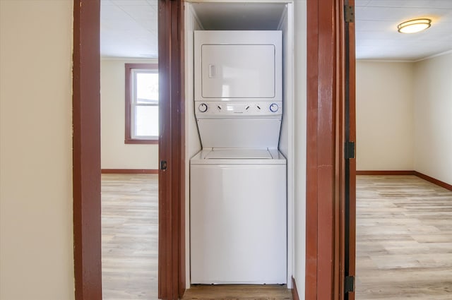 laundry room with light wood-type flooring, stacked washing maching and dryer, laundry area, and baseboards