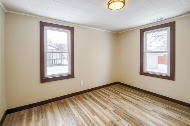 empty room featuring ornamental molding, light wood-style floors, plenty of natural light, and baseboards