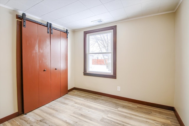 unfurnished bedroom with crown molding, a closet, visible vents, light wood-type flooring, and baseboards