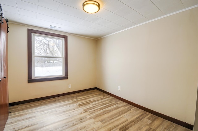 empty room with ornamental molding, a barn door, light wood-type flooring, and baseboards