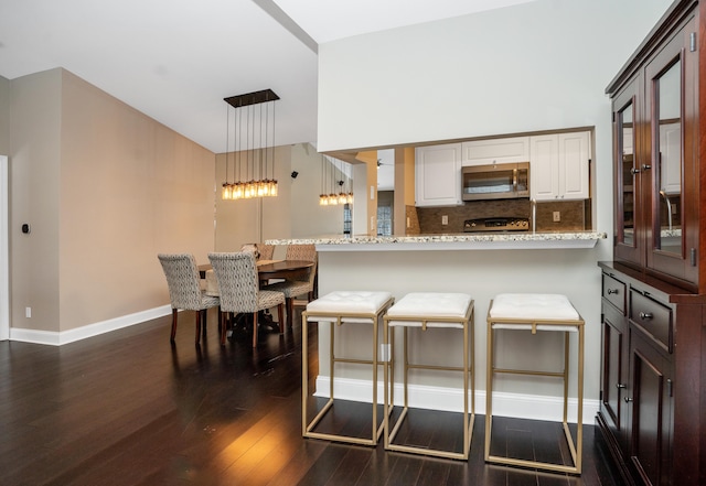 kitchen featuring white cabinets, a peninsula, stainless steel microwave, and a breakfast bar