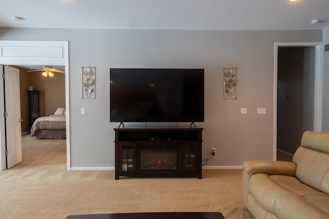 living room featuring light carpet, baseboards, a ceiling fan, and a glass covered fireplace