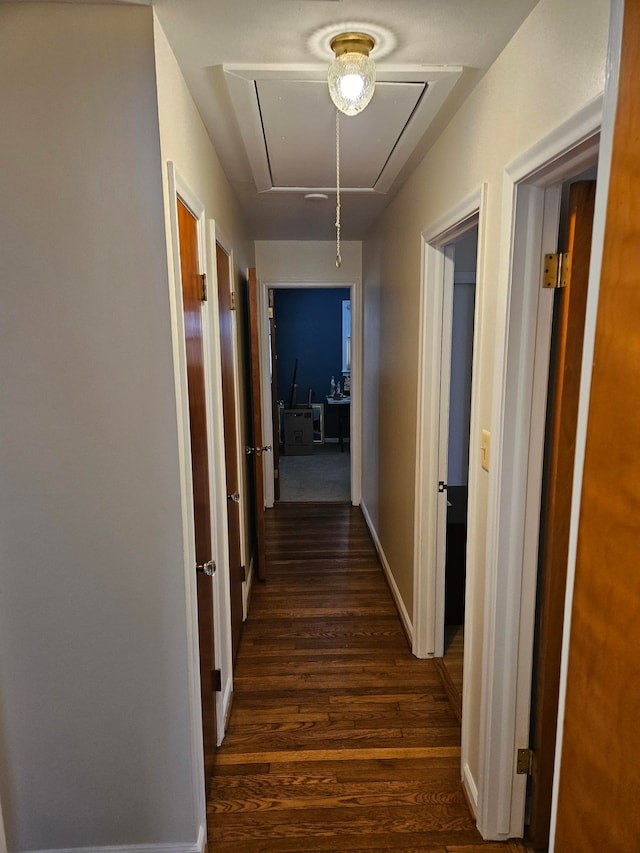 corridor with attic access, dark wood-type flooring, and baseboards