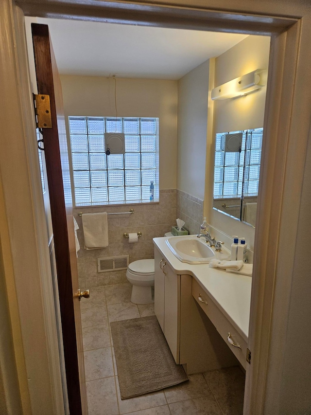 half bath featuring tile walls, visible vents, toilet, vanity, and tile patterned flooring