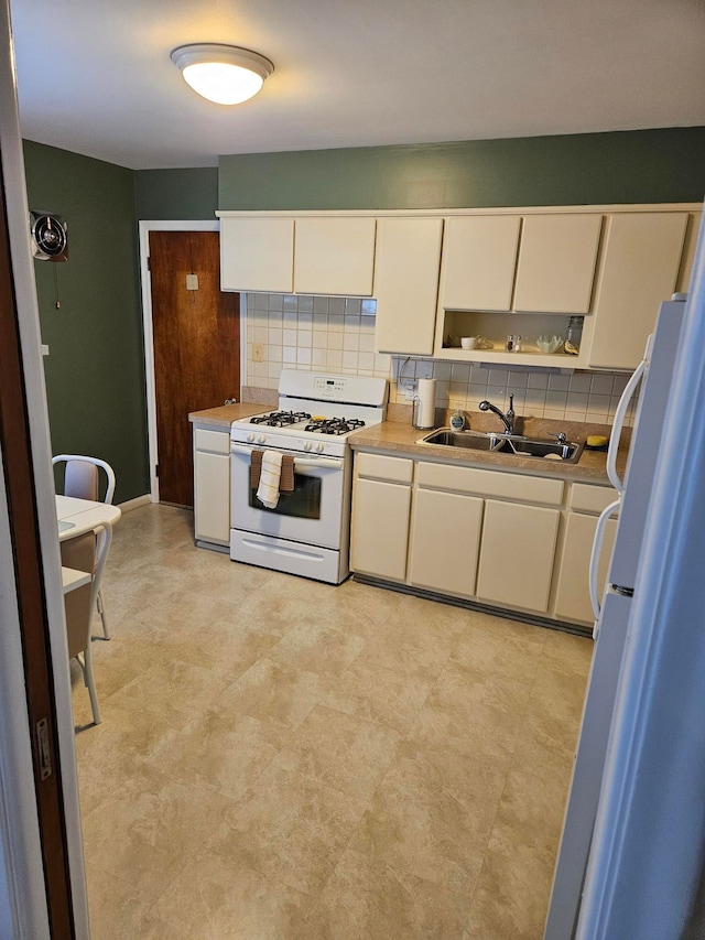 kitchen featuring a sink, white range with gas cooktop, light countertops, freestanding refrigerator, and tasteful backsplash